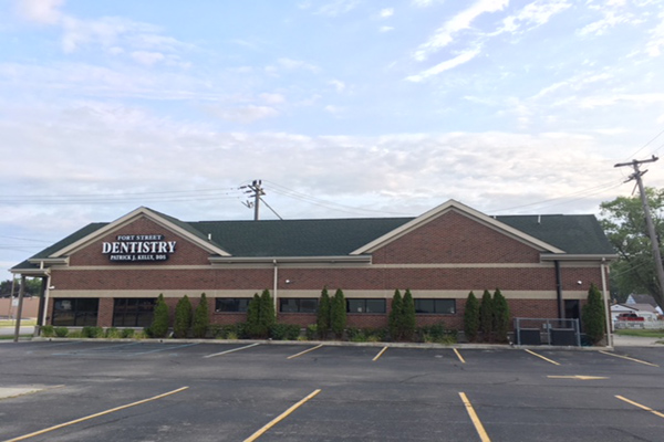 The image shows a building with a sign that reads  DENTISTRY  and the name  DENTISTY  is prominently displayed. The building has a brick facade with a green roof, and it appears to be a professional office setting.