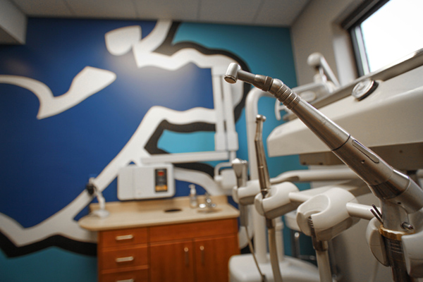 The image shows an interior view of a dental office, featuring a large wall mural with a horse and rider motif, a dental chair with adjustable headrest, and a modern dental equipment setup.