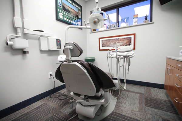 Dental office with a chair in the foreground, dental equipment behind it, and a window with a view of the outside.