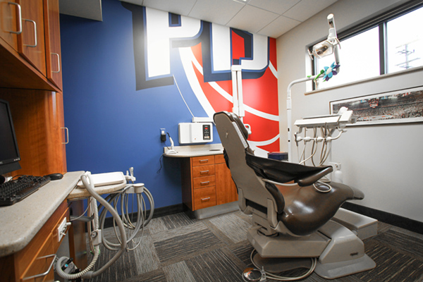A dental office featuring a chair and a desk with a computer, in front of a wall with a large logo.