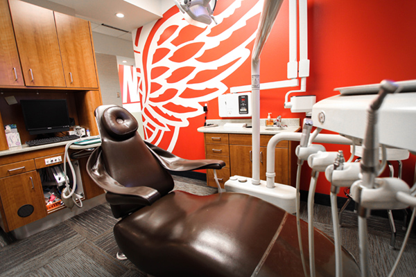 The image depicts an interior space that appears to be a dental office, with a dental chair in the foreground and a sports team logo on the wall behind it.