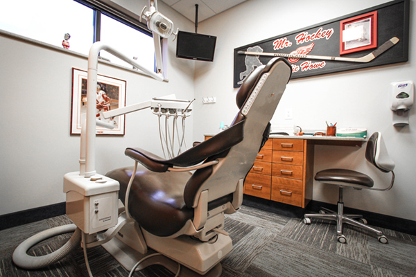The image shows a dental chair with a patient s headrest in an office setting, featuring dental equipment and a sign that reads  We are teaching.