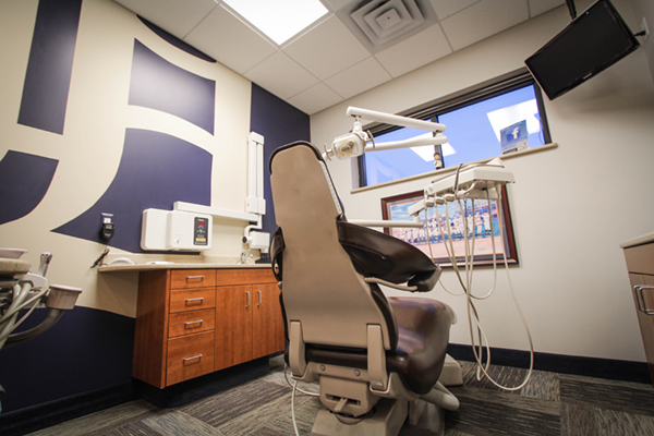 The image shows an interior view of a dental office with a chair and a computer monitor.