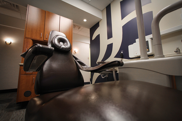 An image depicting a dental chair and an examination room with a high-backed chair, a dental chair, and a countertop with various equipment.