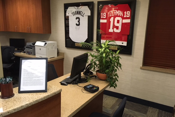 The image shows a professional office environment with framed sports jerseys on the wall behind a desk, featuring names and numbers.