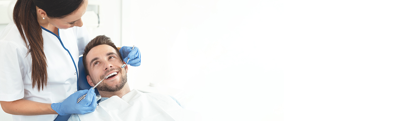 The image shows a dental professional performing an examination on a patient s teeth, with the patient seated in a dental chair and wearing protective glasses.