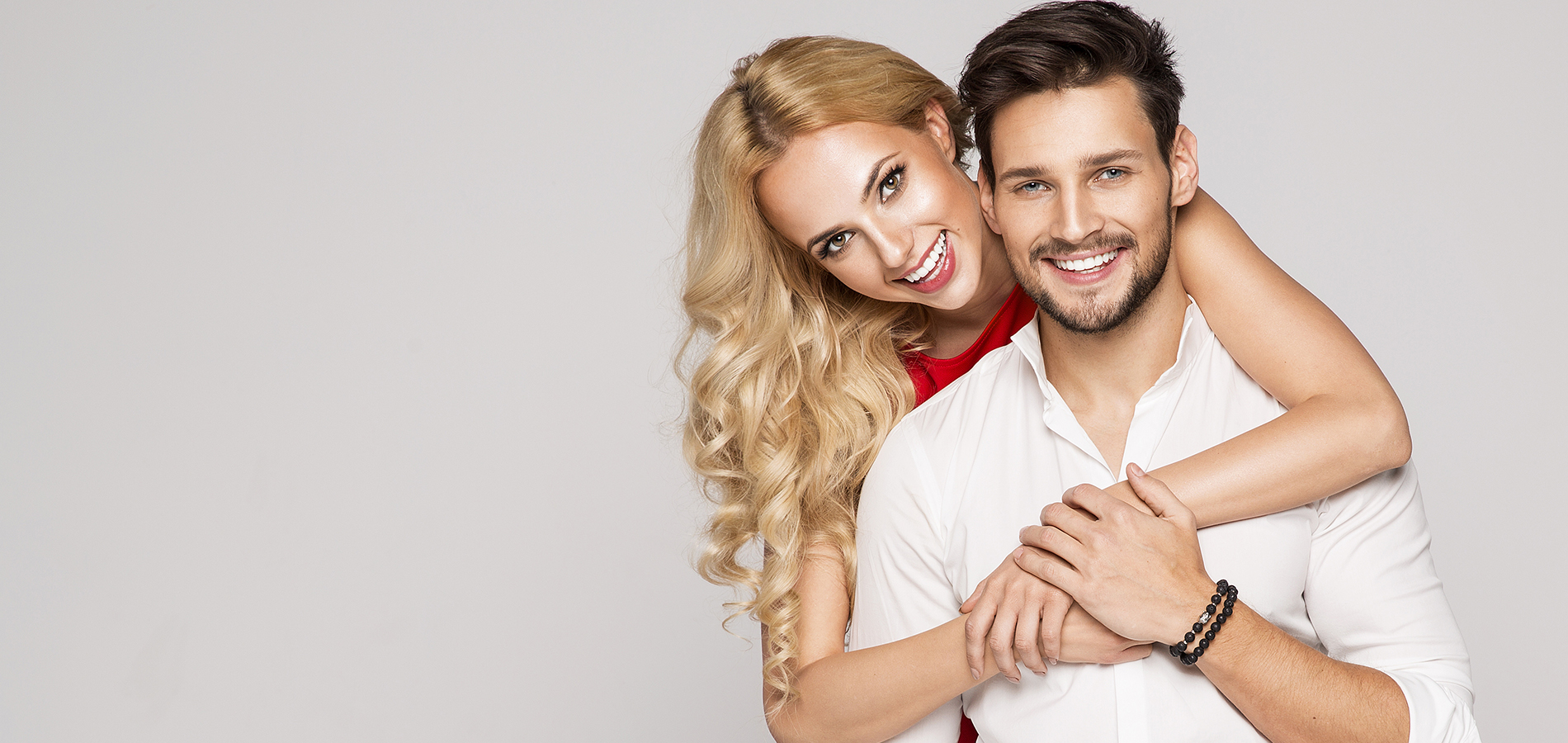 A man and a woman posing together, with the man s arm around the woman, both smiling and appearing happy against a plain background.