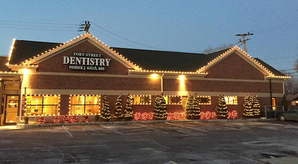 The image shows a building with a sign that reads 'DENTISTRY' and the name 'Parker Dental.' It appears to be an exterior view of a dental clinic at night, with holiday lights and decorations visible.