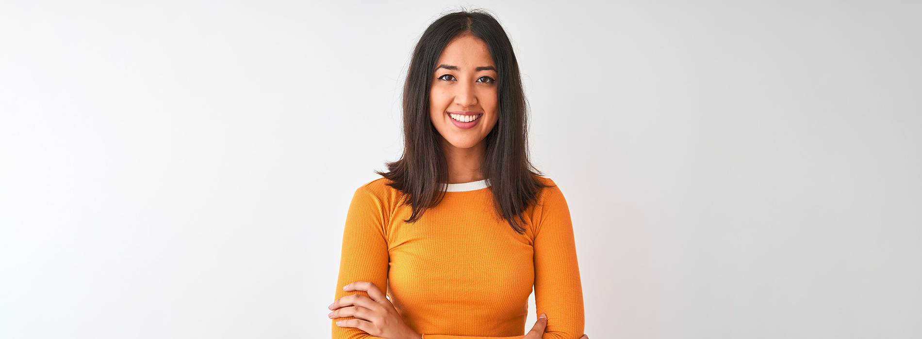 A woman in an orange top stands confidently against a white background.