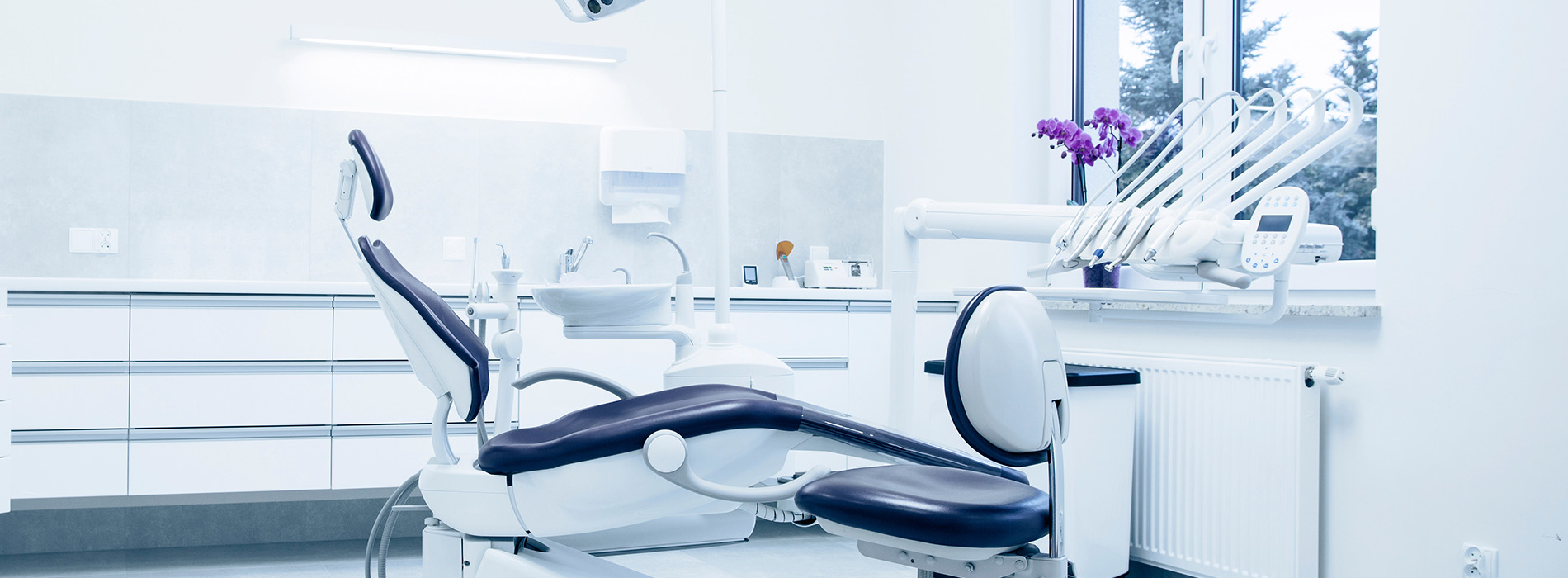 The image shows a modern dental office with a chair, a desk, and various equipment typically found in such a setting.