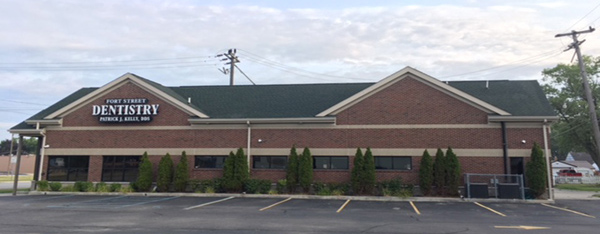 The image shows a two-story building with a sign that reads  Dentistry  on the front, situated in a parking lot with a clear sky.