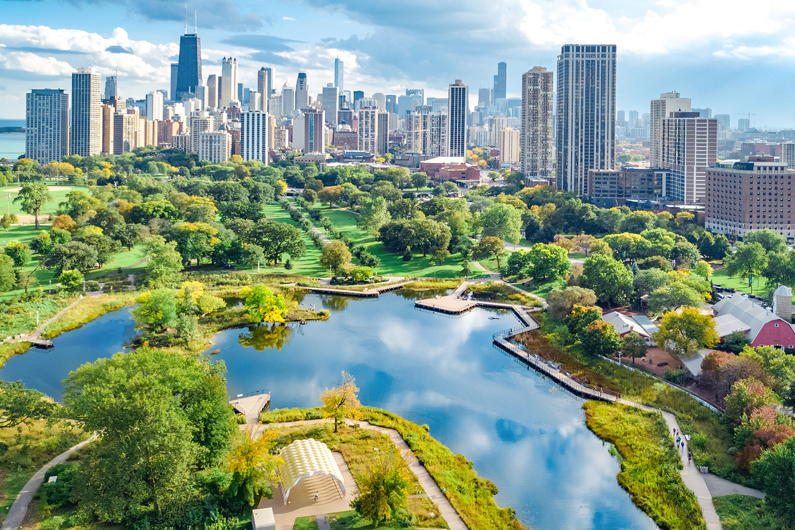 Aerial view of a city park with a lake, skyline in the background, and green spaces.