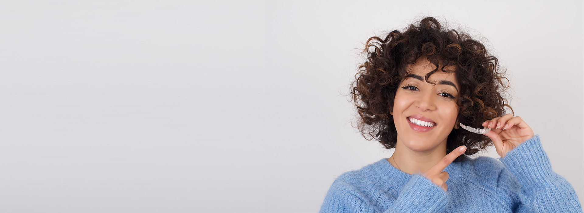 A woman with short curly hair smiling at the camera, holding a phone to her ear.