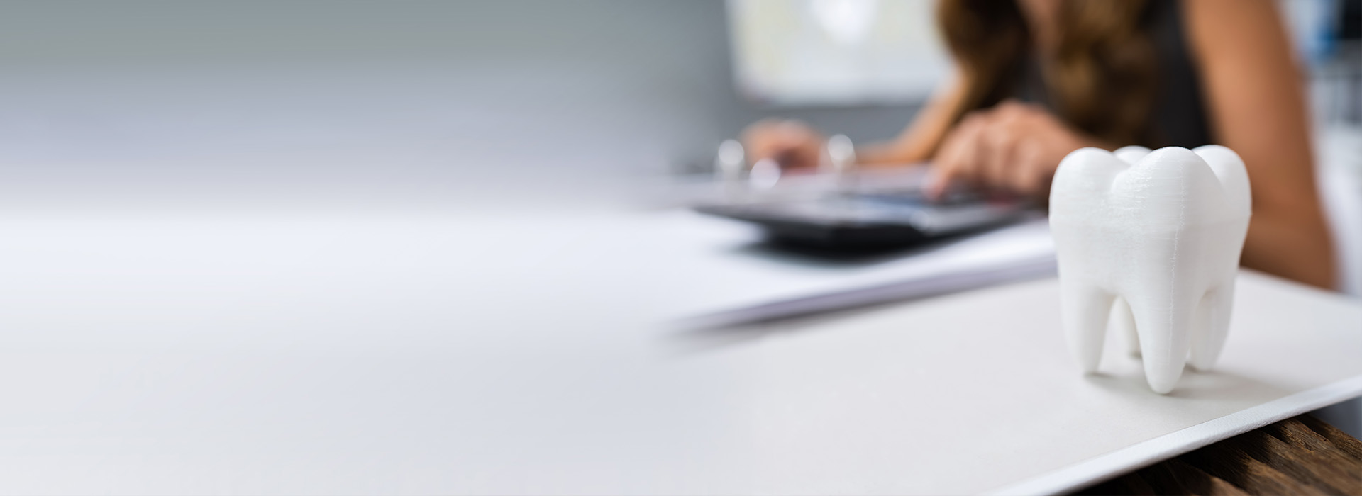 A person working at a desk with a laptop and papers, set against a blurred background.