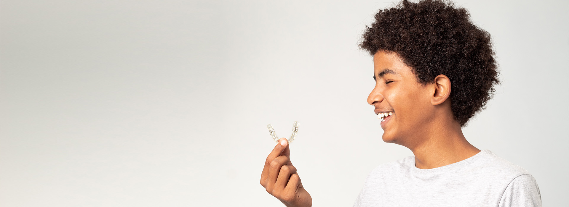 The image features a smiling individual, possibly a child or young adult, holding a small object with both hands, against a plain background.