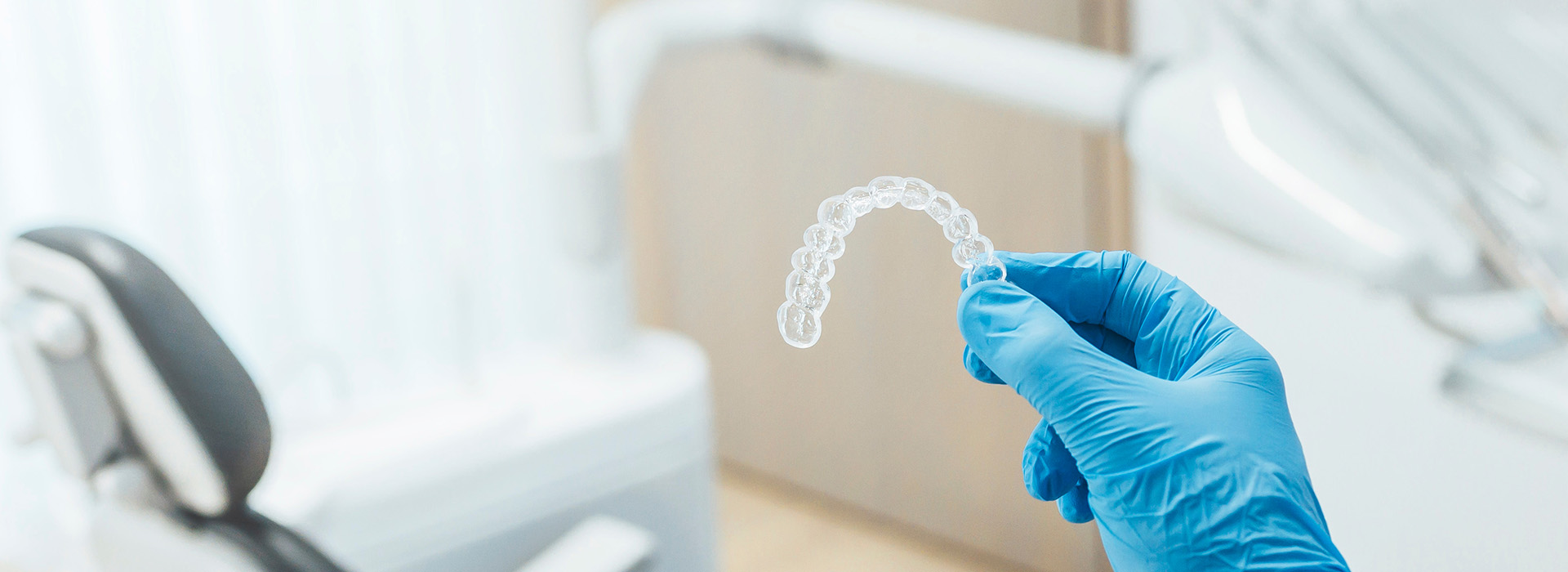 The image shows a close-up of a transparent dental impression material being held by a person wearing blue gloves, with the background featuring a dental office setting.