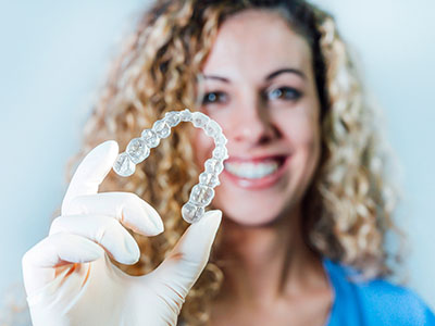 A smiling woman holding a transparent dental retainer with a visible tooth impression.