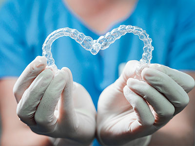 A dental professional s hands holding a clear, heart-shaped dental retainer against a blue background.