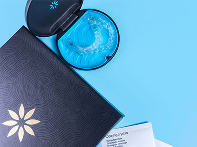 A blue toothbrush and a black box with a logo on top, placed against a light blue background.