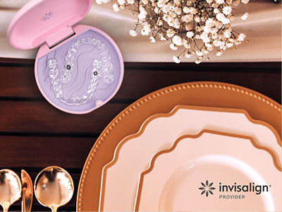 A close-up photograph of a table setting featuring plates, bowls, and a pink cosmetic item with the text  Invisalign  visible.