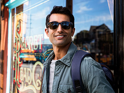 A man in sunglasses and a backpack, standing outside a shop window.