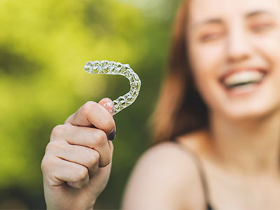 A smiling woman holds a transparent, tooth-shaped object with a playful expression.