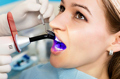 The image features a woman in a dental chair receiving a teeth cleaning with a device that sprays water, while a dental hygienist uses a handheld tool to clean her teeth.