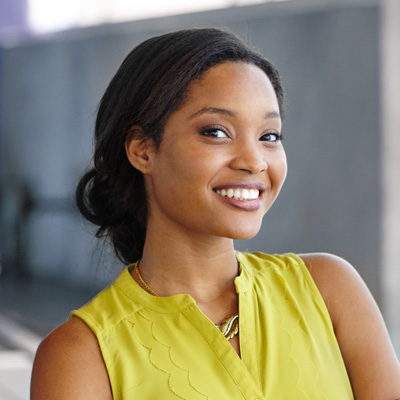 A young woman in a yellow top with a broad smile, posing for the camera.
