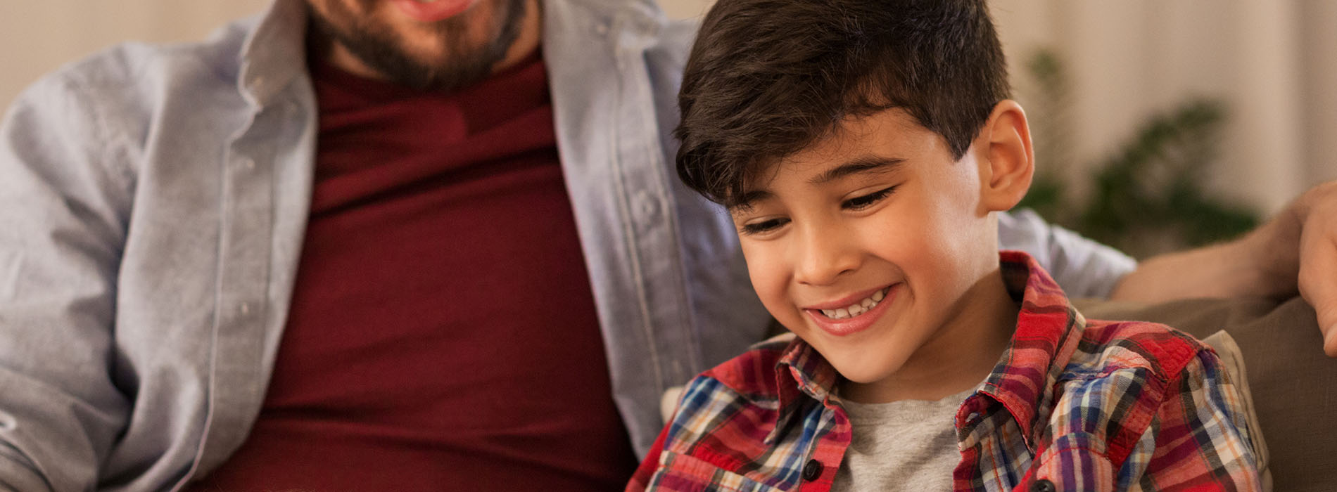 The image shows a man and a young boy sitting on a couch, both smiling at the camera.