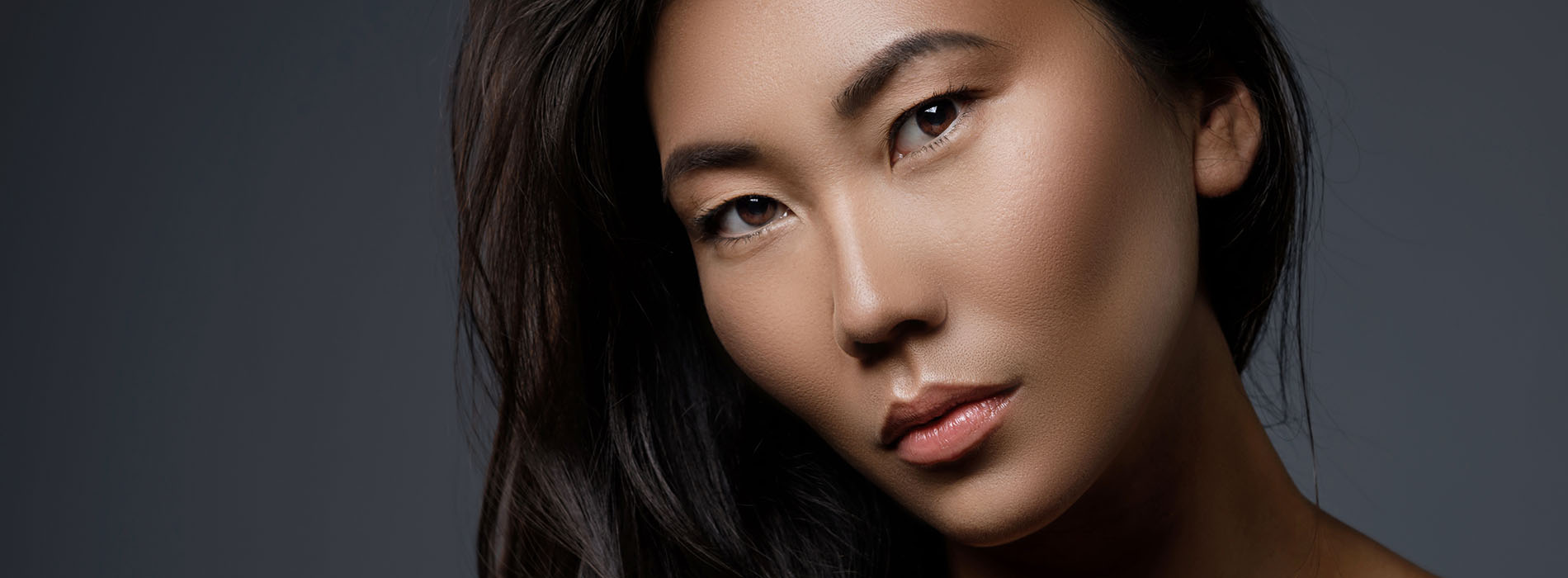 The image features a woman with a neutral expression, looking directly at the camera. She has dark hair and is wearing makeup that includes lipstick. Her skin tone appears to be medium, and she seems to be of Asian descent.