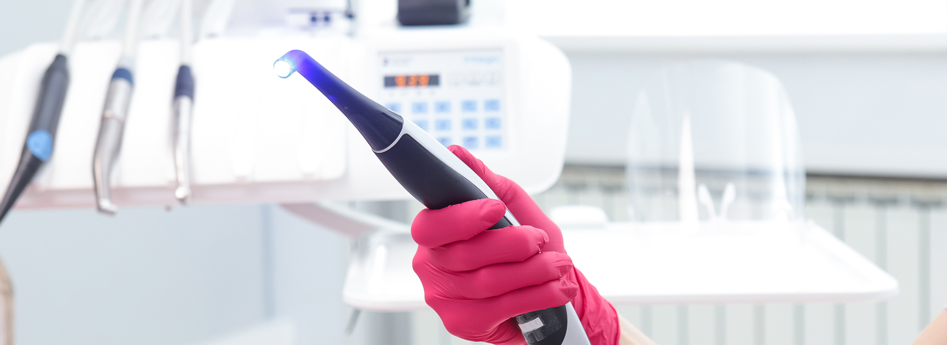 A person holding a blue device, possibly a dental tool or a cleaning instrument, while wearing pink gloves and a red apron in what appears to be a medical or dental setting.