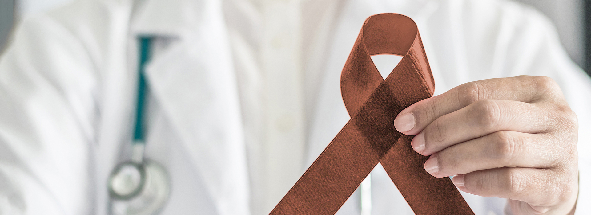 The image features a medical professional holding up a red ribbon with a brown tie on it, set against a background that appears to be a hospital or medical setting.