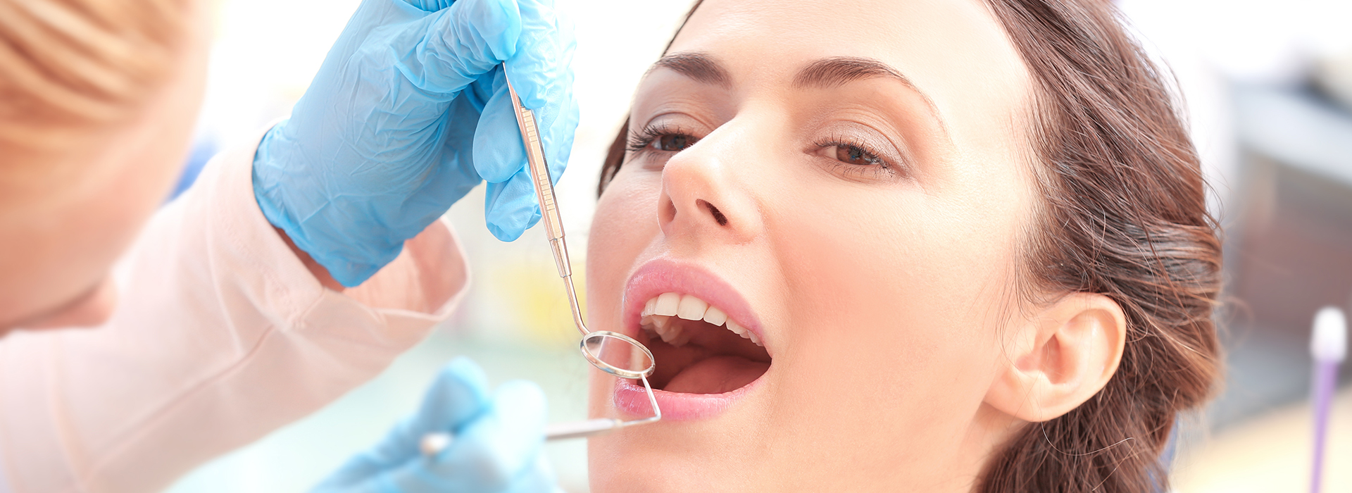 A woman receiving dental care with a dentist using a drill and a handheld mirror.