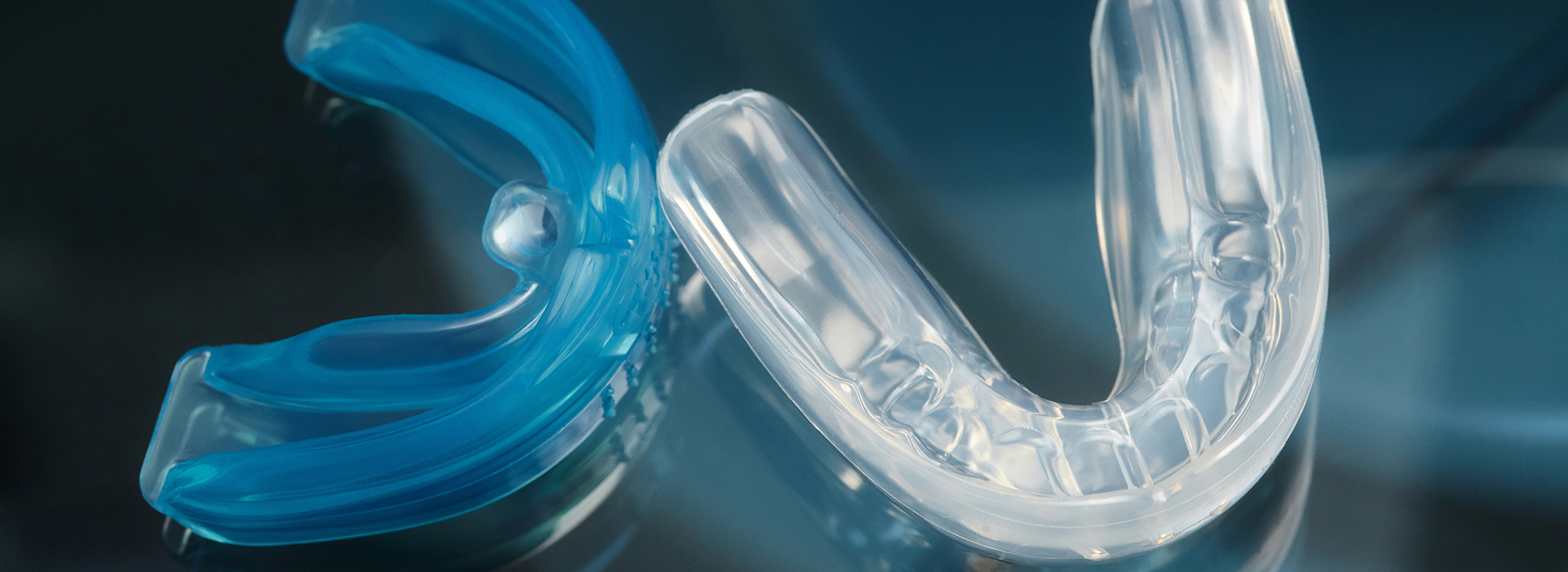 The image shows a clear plastic dental retainer with blue accents, displayed against a blurred background.