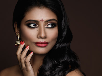 A woman with dark hair, wearing makeup and a red lipstick, poses against a dark background.