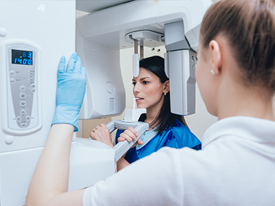 Woman in blue medical gown standing beside a large, modern CT scanner machine.
