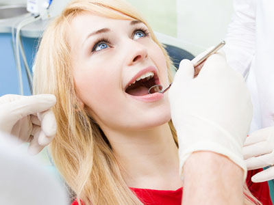 The image shows a woman in a dental chair receiving dental treatment, with a dentist performing the procedure and wearing protective gloves.