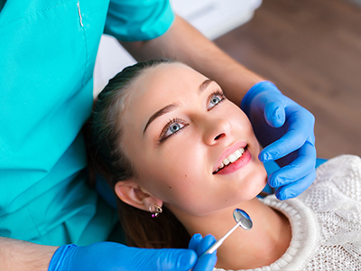 The image shows a woman receiving dental care, with a dentist performing a procedure on her teeth while she is seated in a dental chair.